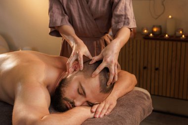 Sakallı adam sıcak ışıklandırması ve huzurlu atmosferi olan sıcak spa odasında kafa masajı yapıyor..