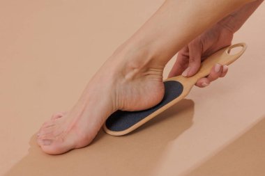 Topuğu düzleştirmek için ayak dosyasını kullanan bir kadın. Tarafsız bir bej arka planda pedikür, cilt bakımı, cilt bakımı ve güzellik anlayışı..