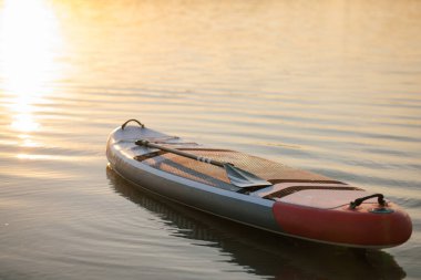 Gün batımında durgun suda kürek çeken şişme raket sükuneti, özgürlüğü ve yaz gölü sporlarının güzelliğini temsil ediyor..