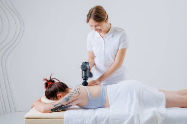 Skolyoz tedavisi ve omurilik bozukluğu düzeltme tedavisi için masaj silahı kullanan bir rehabilitasyon uzmanı..