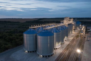 Zirai ihracat ve lojistik için demiryolu ile büyük aydınlatılmış tahıl ambarları ve modern asansör tesislerinin gece görüşü.