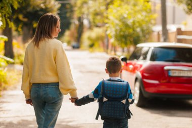Anne ve oğul el ele yürüyorlar okula, sırt çantasına, sabah rutinine, açık havaya, aile desteğine, okul sezonuna