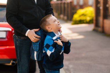 Baba, okula döndüğü ilk gün sırt çantasıyla oğlunu destekliyor. Çocuk bakıyor, aile zamanı, okul hazırlığı, açık hava.