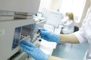 Scientist in protective gloves placing vial in lab analyzer for medical research and diagnostics in a sterile laboratory setting