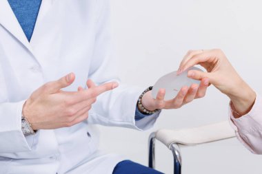 Göğüs implantı gösteren ve hastaya meme büyütme ve düzeltmeyi açıklayan estetik cerrah