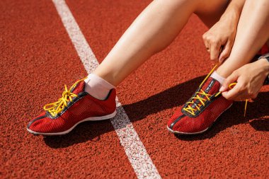 Kırmızı koşu pistinde bağcıklarını bağlayan sporcuları kapatın. Açık hava antrenmanına ve sağlıklı yaşam tarzına hazırlanın..