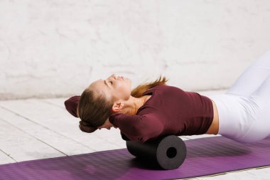 Kas iyileşmesi için köpük silindiri kullanan atletik kadın ve egzersiz sonrası yoga minderinde dinlenen sırt ağrısı.
