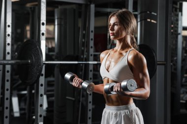 Kendine güvenen atletik kadın, spor salonunda halterleri kaldırıyor, vücut çalışıyor, güçlü kollar formda, motivasyon ve sağlıklı bir yaşam tarzı.