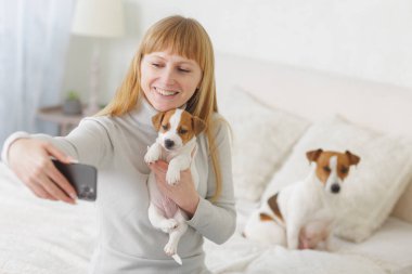 Birlikte selfie çeken yavru köpekle gülümseyen kadın hayvanlara, hayvan bakımına, bağ kurmaya ve evdeki mutlu anlara sevgi gösteriyor..