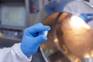 Eldiven işçisi steril ilaç üretim tesisinde kalite kontrolü sırasında tek bir hapı kontrol ediyor.