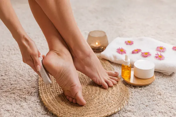 Topukluların üzerinde sünger taşı kullanan kadın nasır aldırma ve yumuşak ayaklar, ev pedikürü ve pürüzsüz cilt için krem ve yağ ile kaplıca bakımı