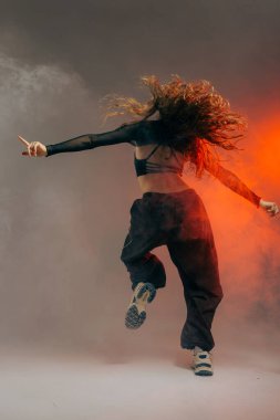 Arkadan çekilen modaya uygun kıyafetli kendinden emin caz funk dansçısı dramatik duman efektleriyle hareket ediyor..