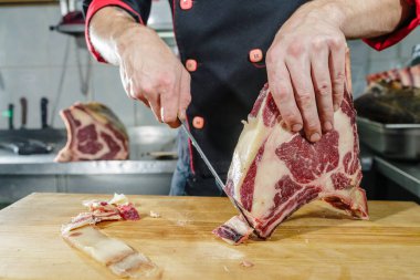 Şef ahşap tahtada kurutulmuş pirzola bifteği kesiyor mutfakta keskin bir bıçakla mermer ve yağ kesme işlemini gösteriyor.