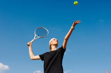 Kendine güvenen genç bayan tenisçi açık havada top oynuyor, aktif yaşam tarzını ve kadın spor yetkilerini teşvik ediyor.