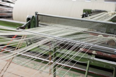 Warp iplikleri, temiz bir endüstriyel değirmende yünlü tekstil üretimi ve hizalanmasını gösteren modern bir dokuma tezgahında sazlığı besliyor..