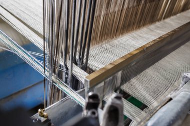 Warp hızını heddles ve Reed 'in uçsuz bucaksız tezgahında yakından görmek, modern bir tekstil değirmeninde yünlü kumaş üretimini gösteriyor..