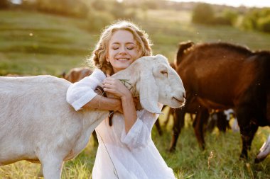 Gülümseyen çiftçi çayırda süt keçisine sarılıyor. Keçi sütü peyniri, organik tarım ve hayvan yardım hikayeleri için ideal.