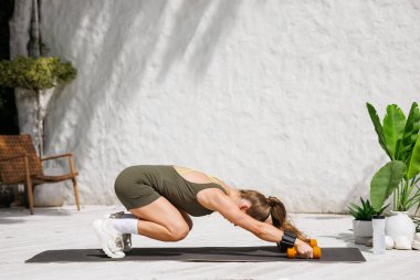 Kadınlar halterleri ve kol ağırlıkları ile bir hasırın üzerinde geriliyor. Modern sahne ısınma hareketleri ve düşük etki gücü içeriği için.