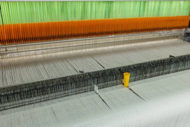 Wide view of a jacquard loom with colored heddles guiding warp threads for precision weaving in a modern textile factory