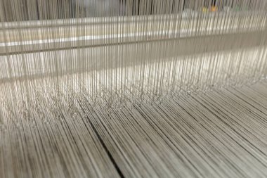 Close view of heddles and warp threads on a modern loom in a textile factory showing precision weaving and quality production