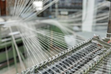 Warp iplikleri rehberler ve gerilim kontrolünden geçer. Bir dokuma tezgahını, hassas kurulum ve üretim kalitesini gösteren bir tekstil fabrikasında besler.