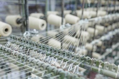Warp yarns pass over guide hooks from creel to weaving line in a textile factory showing tension control and precise setup