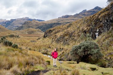 Ekvador 'un dağlık bölgelerindeki Cajas Ulusal Parkı' nda elleri cebinde gülümseyen bir kadın yürüyüşçünün geniş açılı fotoğrafı..