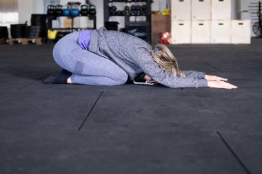 Sarışın, orta yaşlı bir kadının Vinyasa akış yoga antrenmanı sırasında çocuk pozunda dinlenmesi ve spor kıyafetlerini spor salonunda giymesi..
