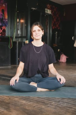 Vinyasa akış yogası sırasında spor giyerken rahat bir şekilde dinlenen gülümseyen yeni yoga öğretmeninin dikey fotoğrafı.