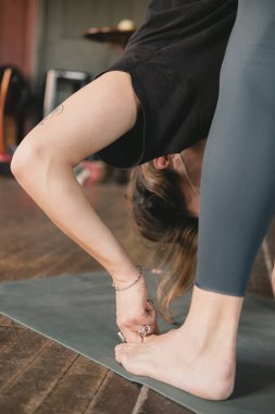 Vinyasa akış yoga pratiği sırasında baş parmaklarını (Padangusthasana) bağlayarak öne doğru poz veren tanınmayan bir kadın yoga öğretmeninin dikey yakın plan fotoğrafı.