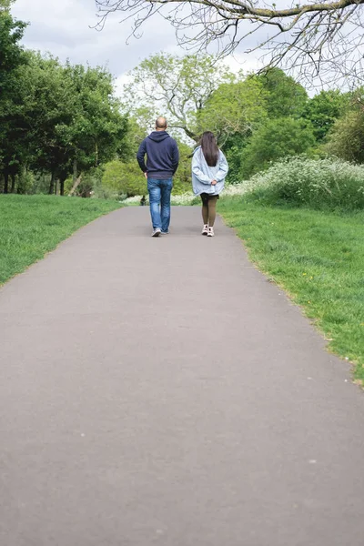 Vertical photo of a multicultural couple walking on a footpath in Figgate Park in Edinburgh in spring time. Multiethnic family.