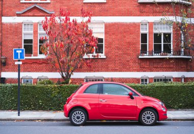 İngiltere 'nin Londra sokaklarında kırmızı ağaçlı kırmızı tuğlalı bir binanın önüne park edilmiş kırmızı küçük bir arabanın yatay fotoğrafı..