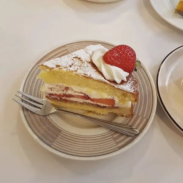 Beyaz bir tabakta çilekli ve kremalı taze pişmiş kek.