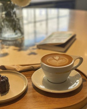 Beyaz arka planı olan ahşap bir masanın üzerinde kapuçino olan bir fincan.