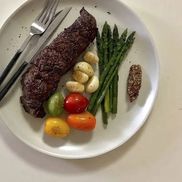 Beyaz tabakta ızgara biftek, sebze ve baharat.