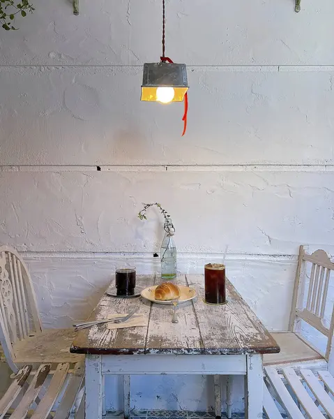 Beyaz lambalı bir masa ve tuğla duvarda bir fincan çay.