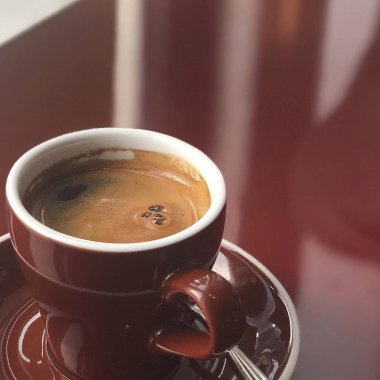 Beyaz fincan tabağı ve arka plandaki ahşap masada bir bardak kahve..