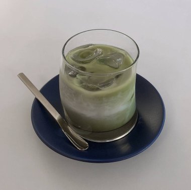 Bir bardak buzlu yeşil çay ve beyaz arka planda bir fincan çay.