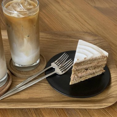 Kahve dükkanı olan ahşap bir masada buzlu kahve ve kremalı kek..