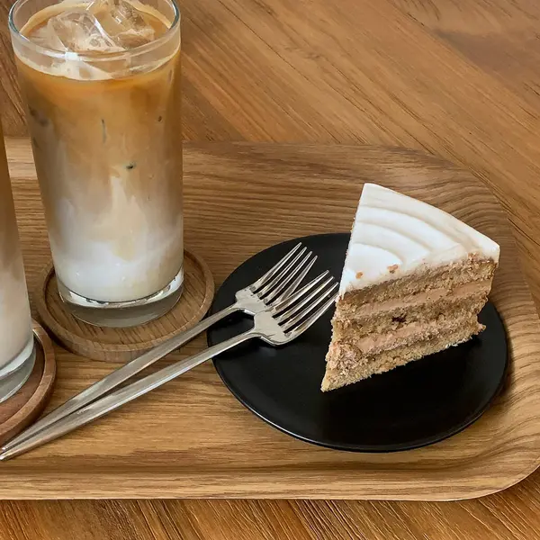 Kahve dükkanı olan ahşap bir masada buzlu kahve ve kremalı kek..