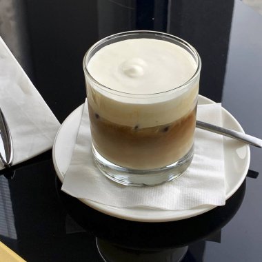 Siyah arka planda beyaz kahve fincanı ve kaşıkla bir bardak süt.