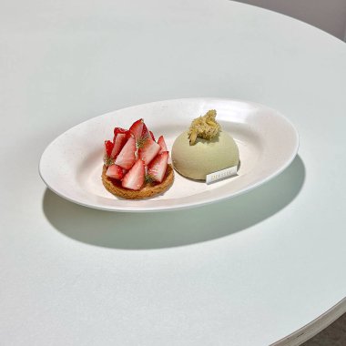 Tabakta bir dilim kek ve masada kaşıkla beyaz bir tabak.