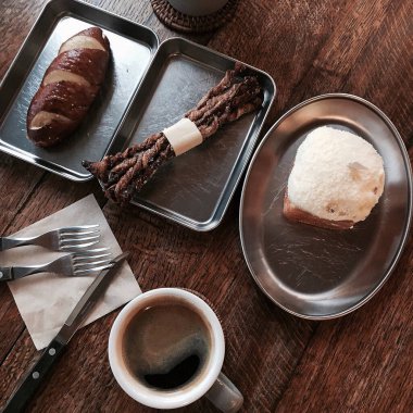 Bir fincan kruvasanla kahve, bir fincan kahve ve tahta bir masada kaşık.