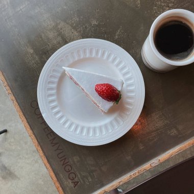 Tahta bir masada beyaz bir tabakta bir fincan kahve ve bir parça kek..