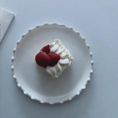 Beyaz arka planda beyaz bir tabakta kırmızı kurdeleli beyaz çikolatalı kekin yakın plan fotoğrafı.