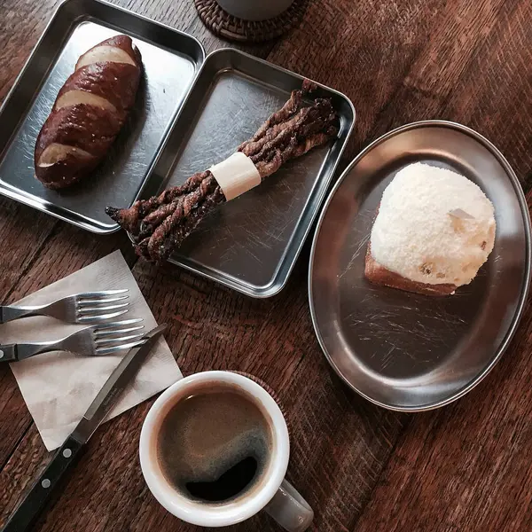 Bir fincan kruvasanla kahve, bir fincan kahve ve tahta bir masada kaşık.