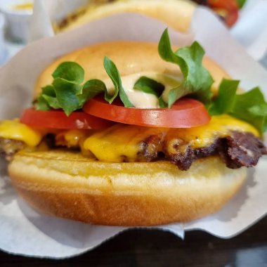 Bir restoranın ahşap masasında üzerinde peynir olan bir hamburgerin yakın çekimi.