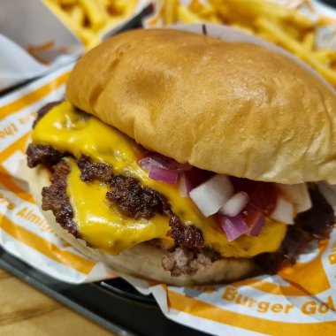 Tahta bir masada patates kızartması ve peynirli leziz hamburgerleri yakın.