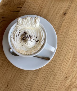 Beyaz bardaklı bir kapuçino ve ahşap bir masada bir çikolata.