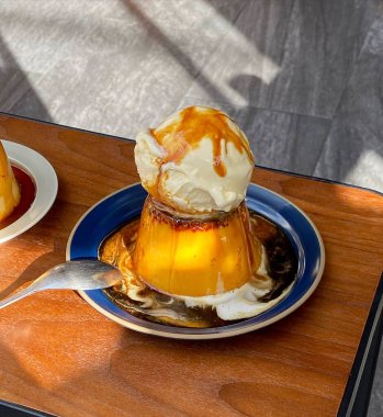 Lezzetli bir karamelli dondurmanın dikey görüntüsü beyaz bardakta bir kaşık ve tabakta bir kaşık.